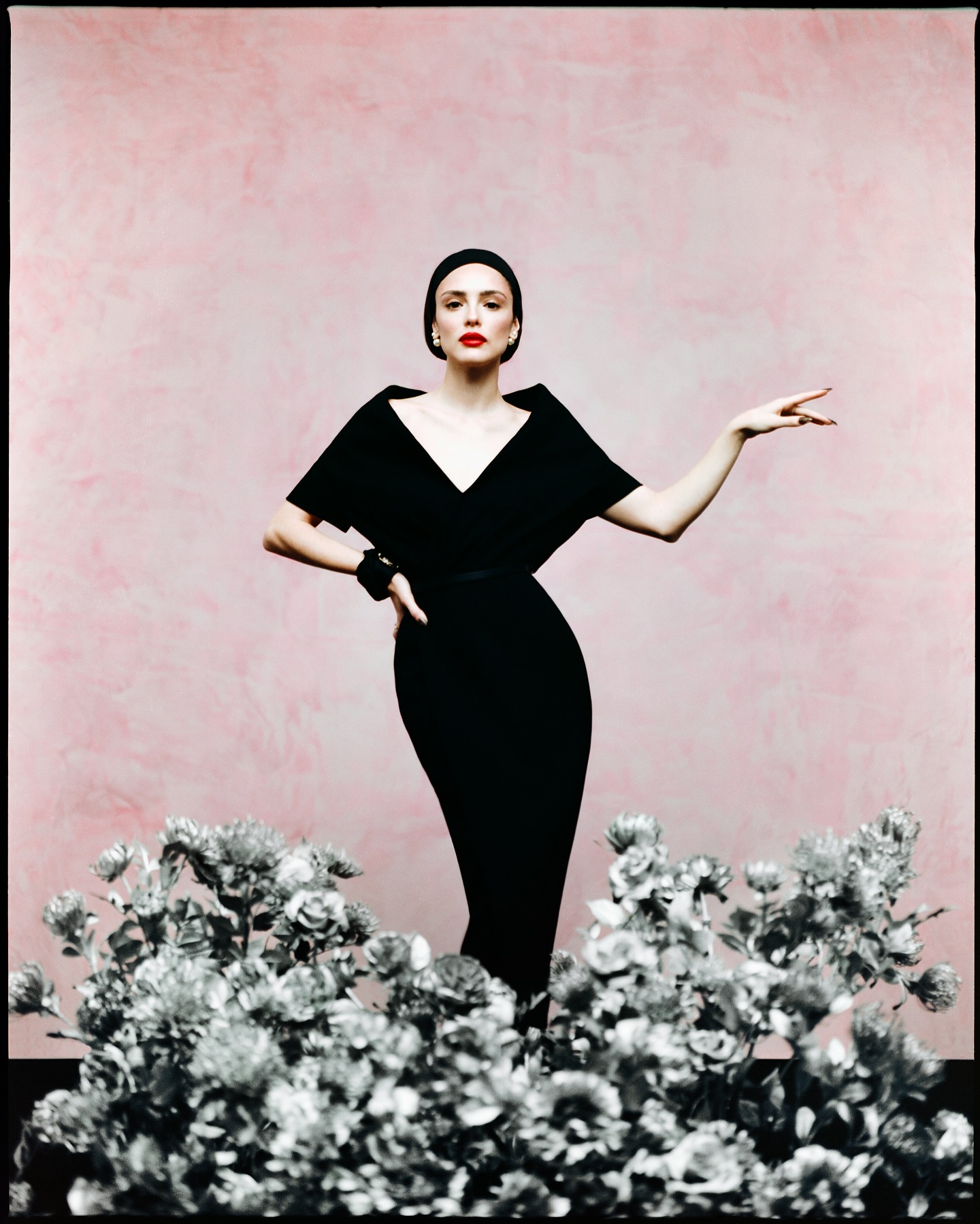 Modelo em vestido preto diante de cenário floral